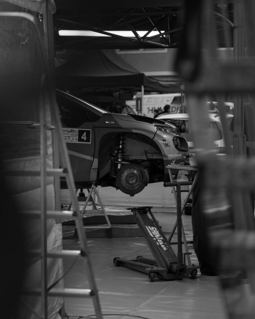 Monochrome image of a car undergoing repair at an indoor automotive workshop.